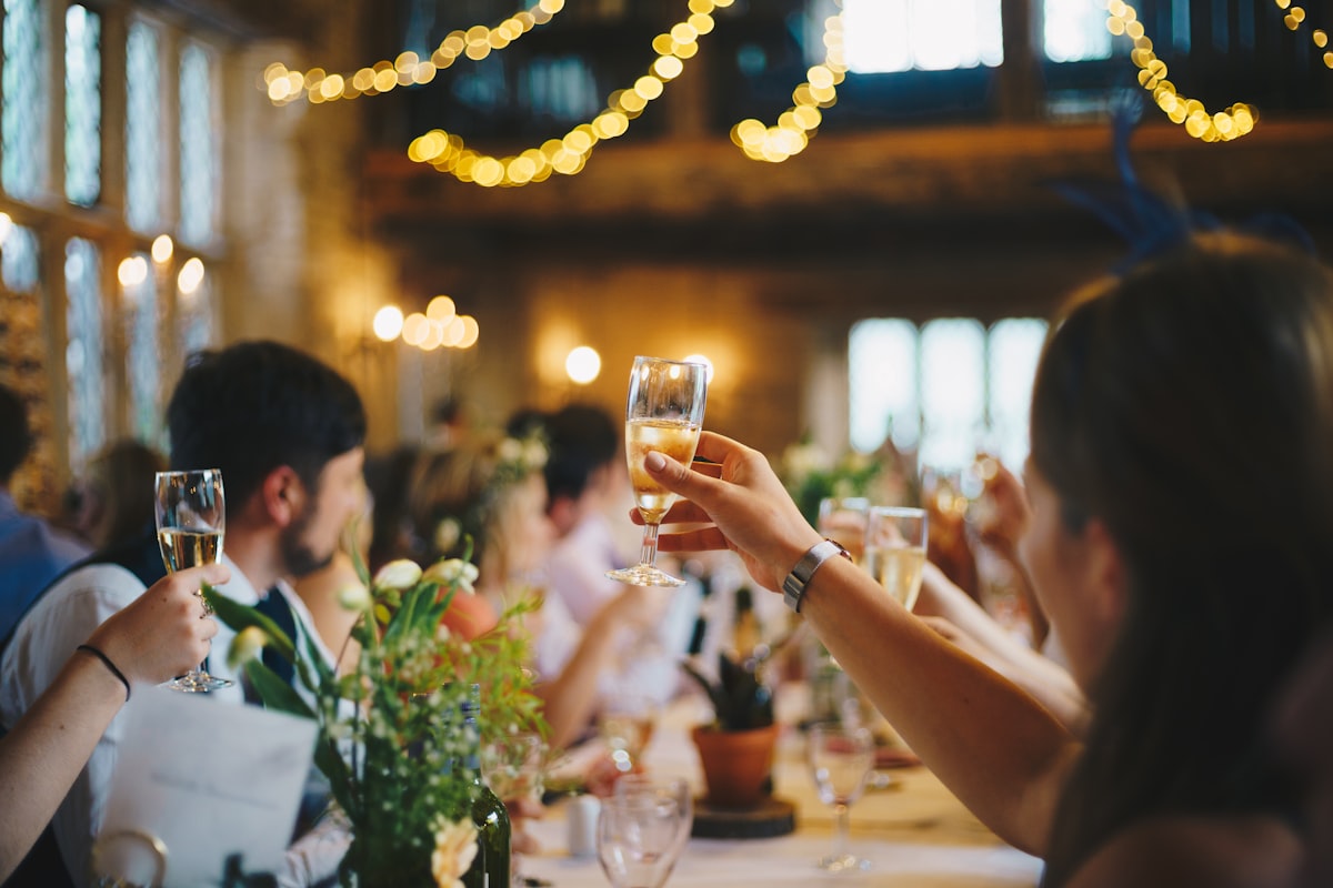 Wedding guests raising champagne glasses in a toast at a table decorated with flowers and string lights
